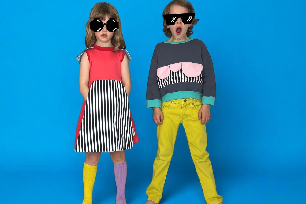 Two children in brightly coloured outfits stood against a blue background