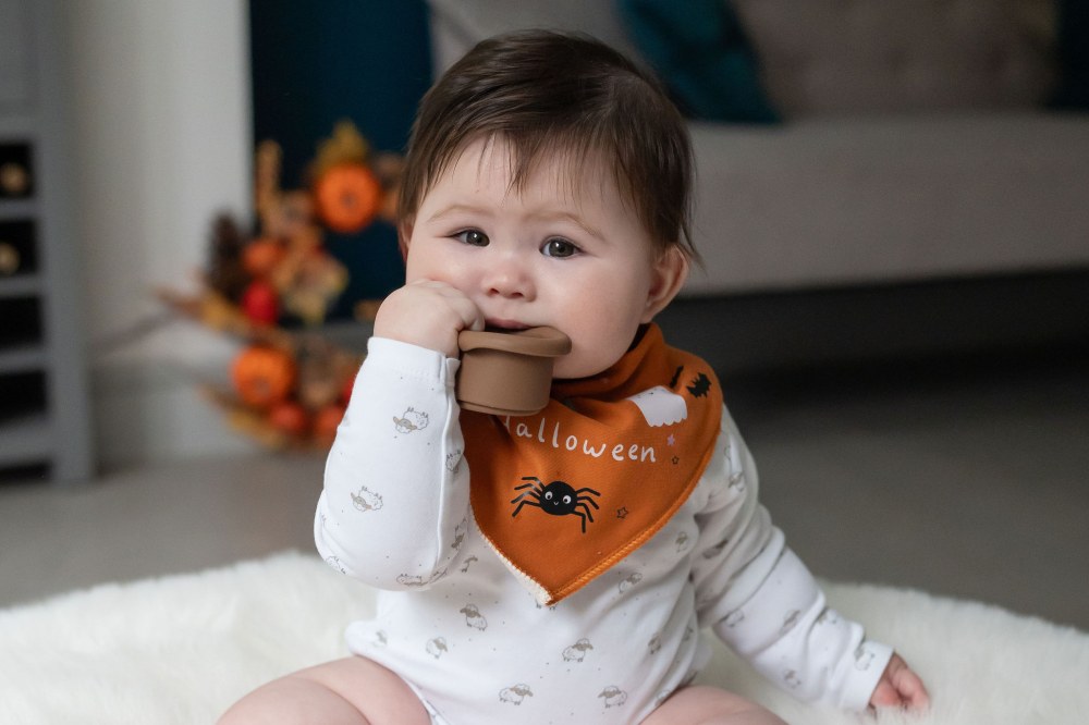 A baby sat on the floor wearing an orange Halloween dribble bib by Ziggle