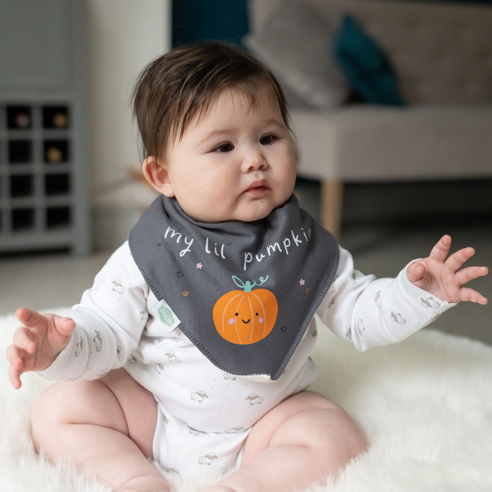 A baby sat on the floor wearing a My Lil Pumpkin Halloween dribble bib by Ziggle 