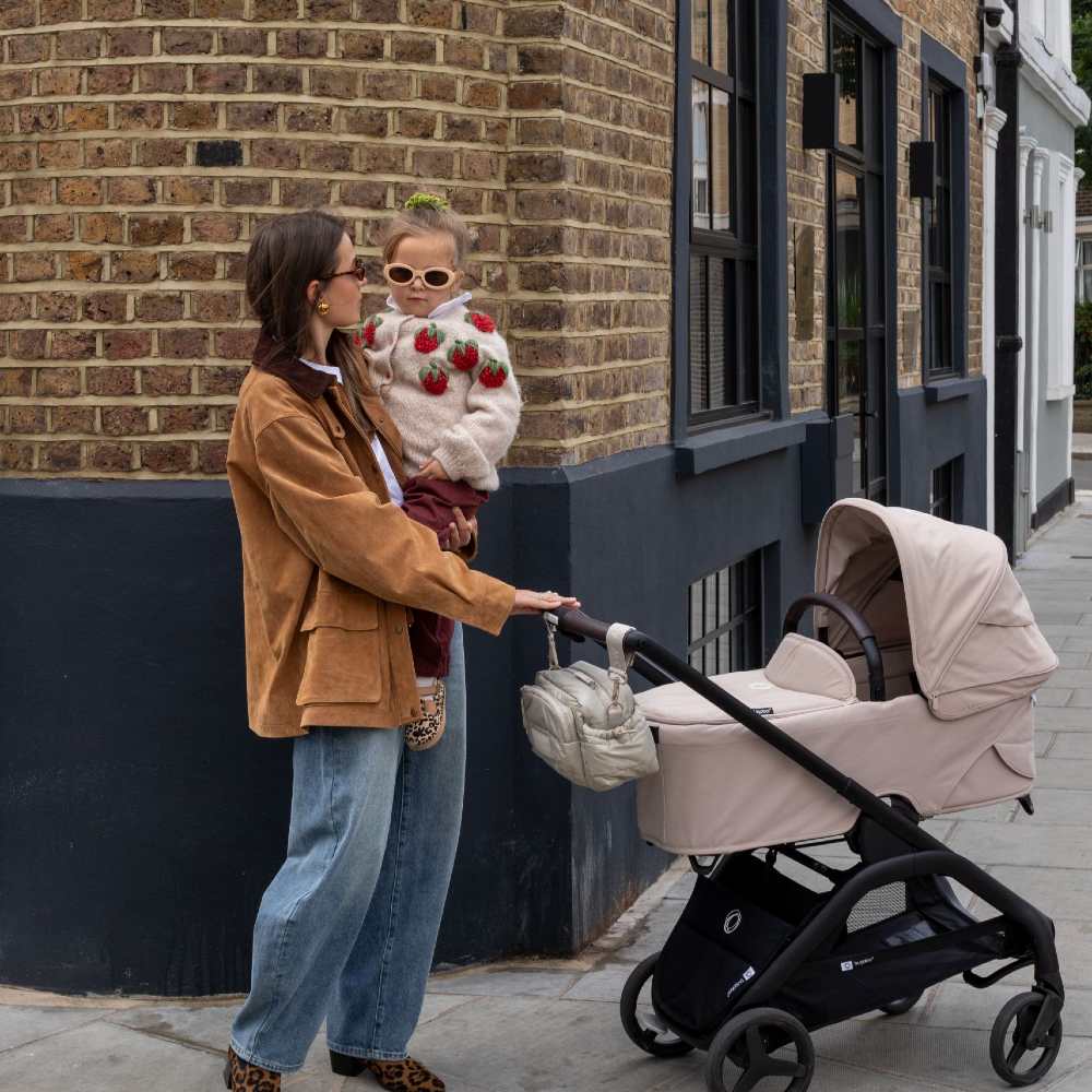 A woman holding a child and a pram with accessories by Avery Row