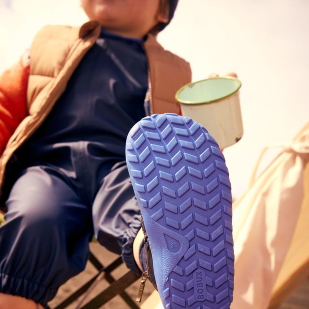 A child sat in a camping chair holding a mug and lifting the sole of their shoe up to the camera
