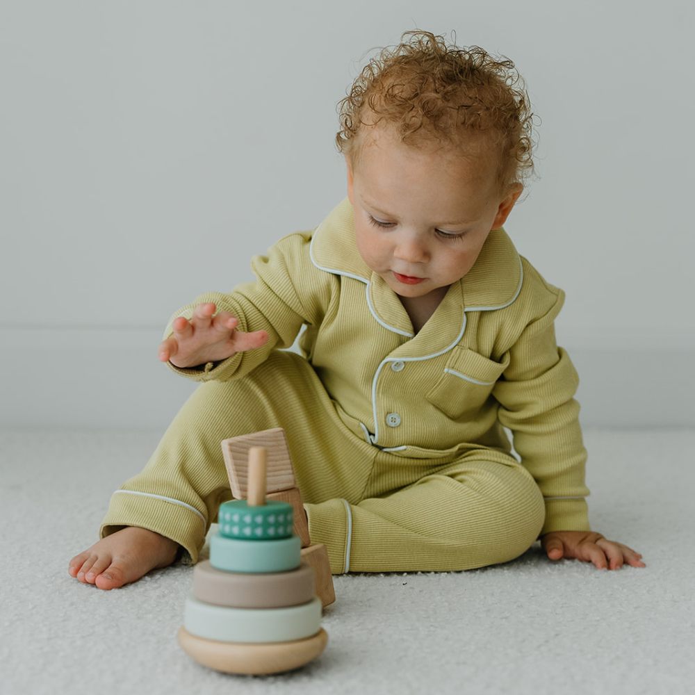 A young child sat on the floor playing with a toy and wearing green pyjamas 