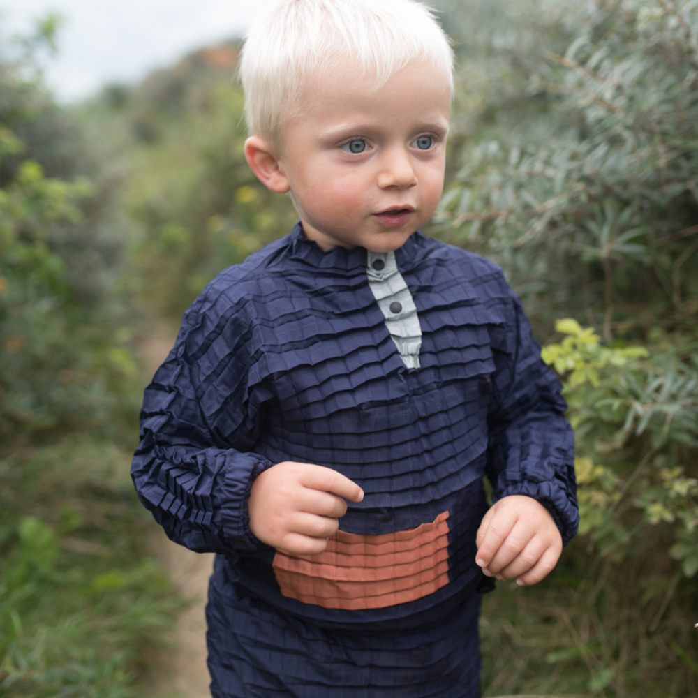 A boy in a blue outfit by Petit Pli walking outside down a path 