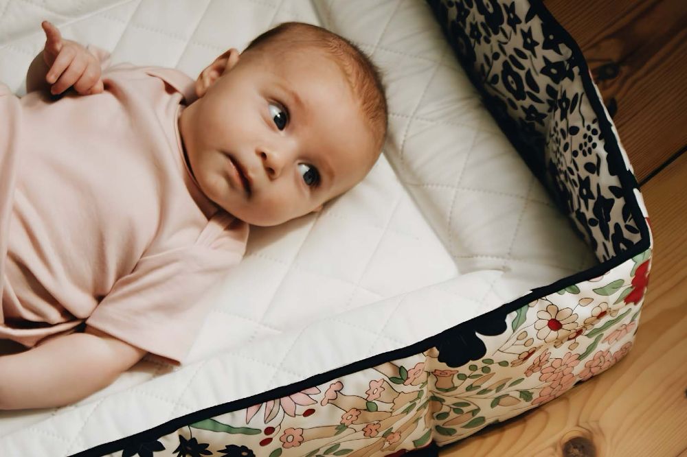 A baby on a changing mat looking at a Liberty print bumper from the Etta Loves x Liberty collection