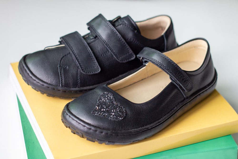 Two black Froddo Barefoot school shoes displayed on top of books