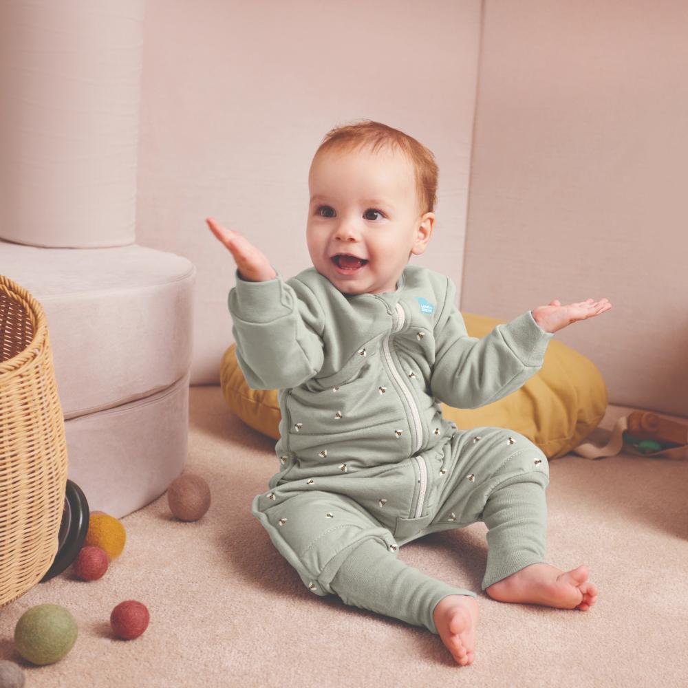 A baby sat on the floor wearing a green sleepsuit 
