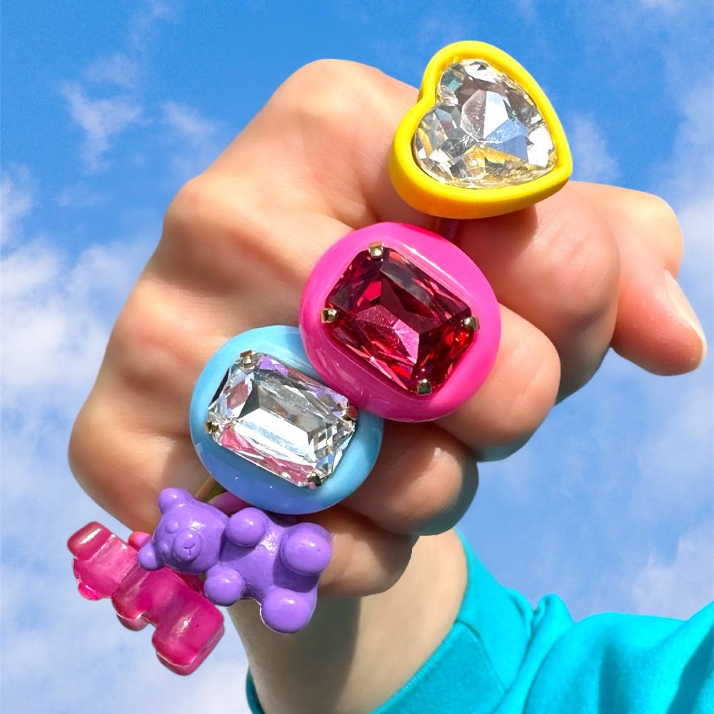 A person's fist wearing brightly coloured gem stone rings 