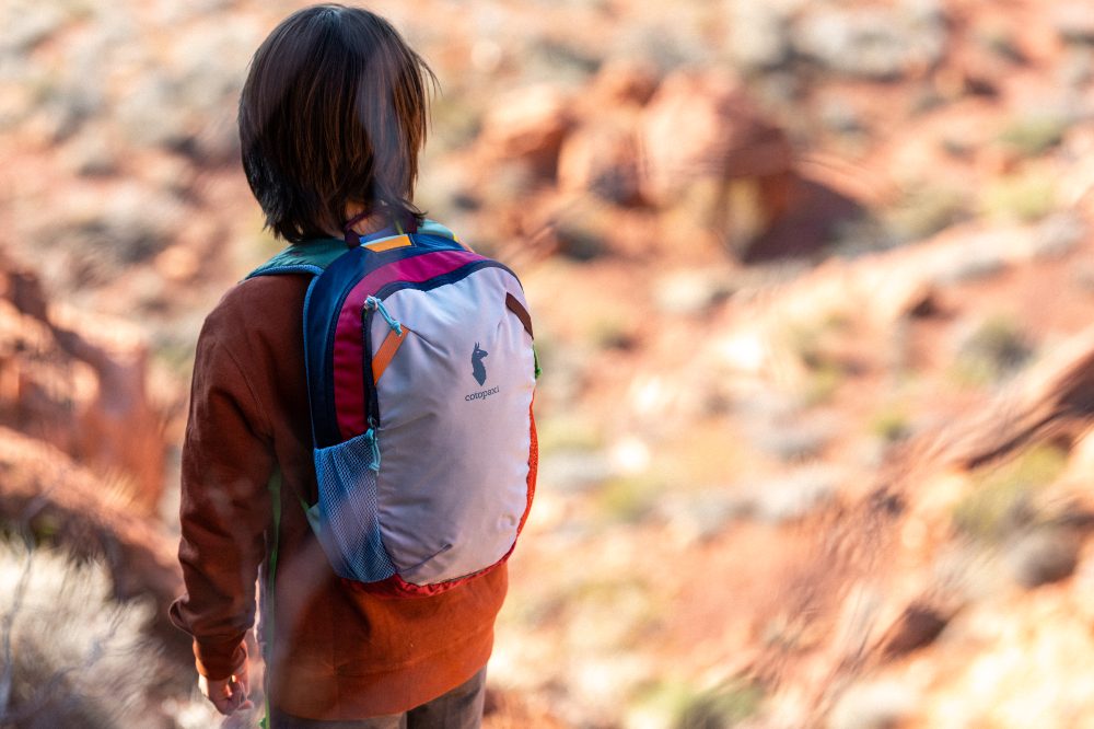 A child stood outside wearing a Cotopaxi backpack