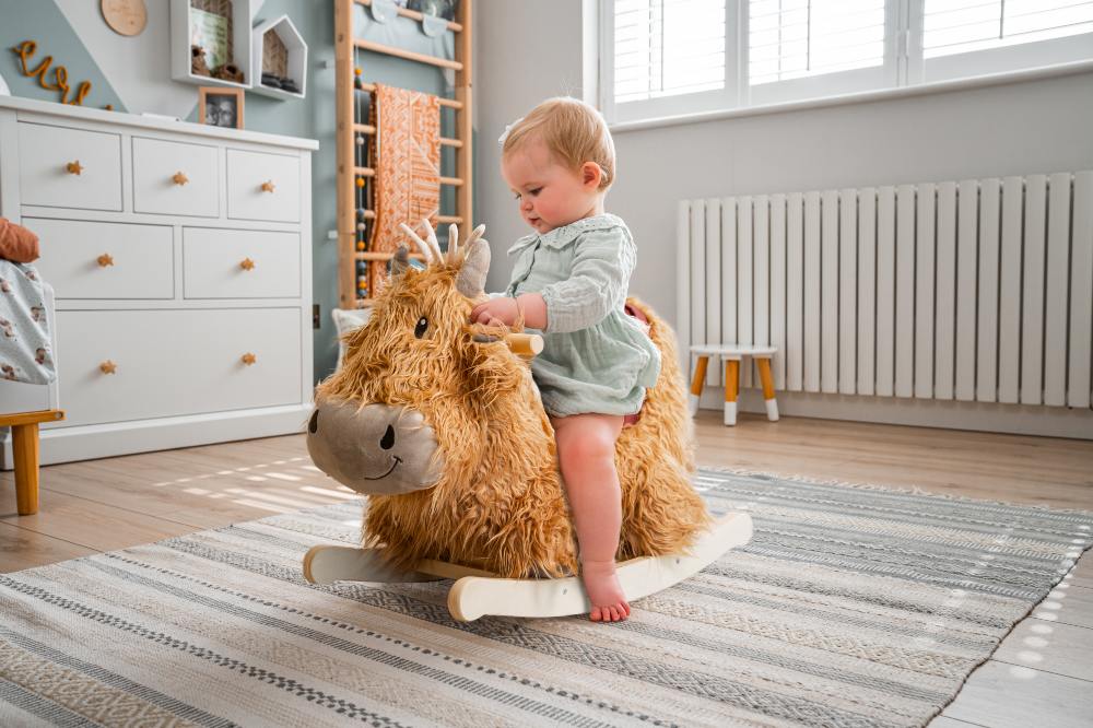 A young child sat on a Highland Cow ride-on toy by The Little Bird Told Me