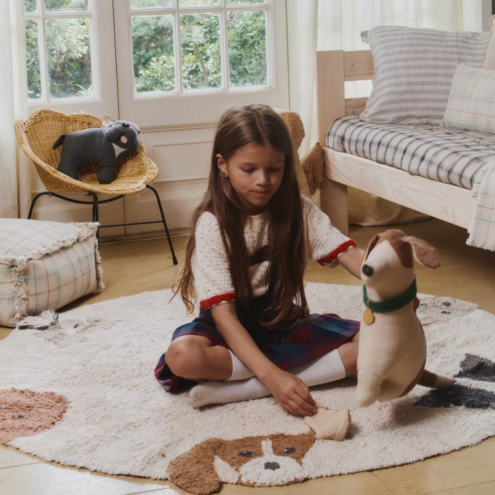 A girl sat on the floor in a room with dog themed baskets and cushions by Lorena Canals