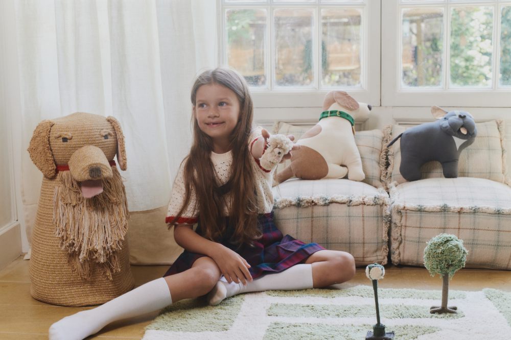 A girl sat on the floor in a room with dog themed baskets and cushions by Lorena Canals