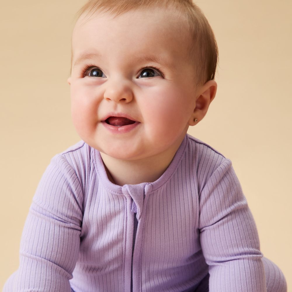A smiling baby wearing a lilac ribbed babysuit by MORI
