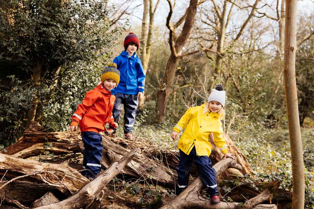 Three children in a wood wearing bright outerwear by Muddy Puddles