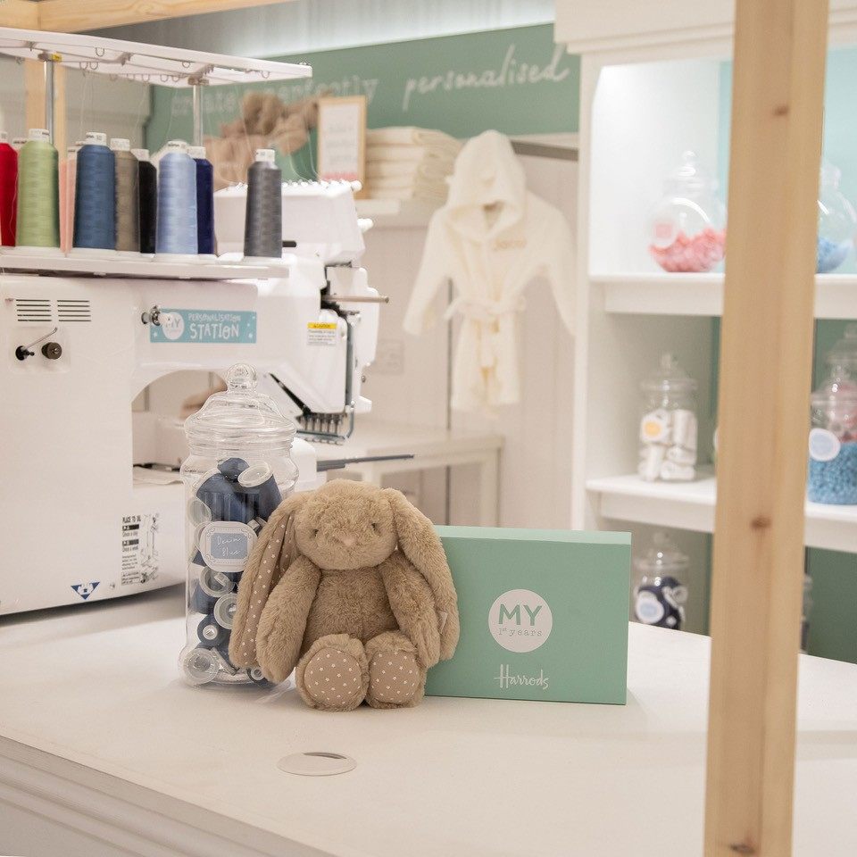 A soft toy on a counter top beside an embroidery machine 