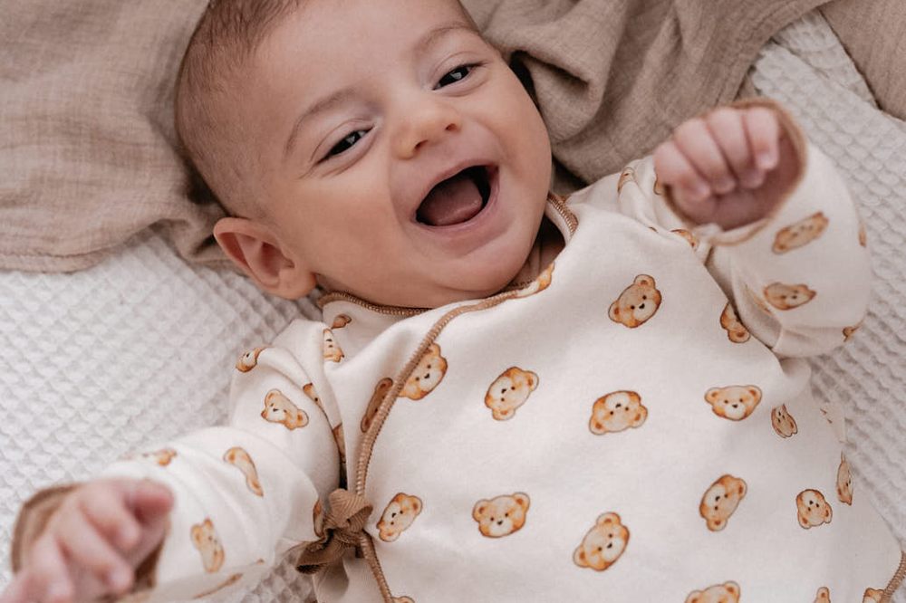 A smiling baby wearing a teddy bear print top by North Baby