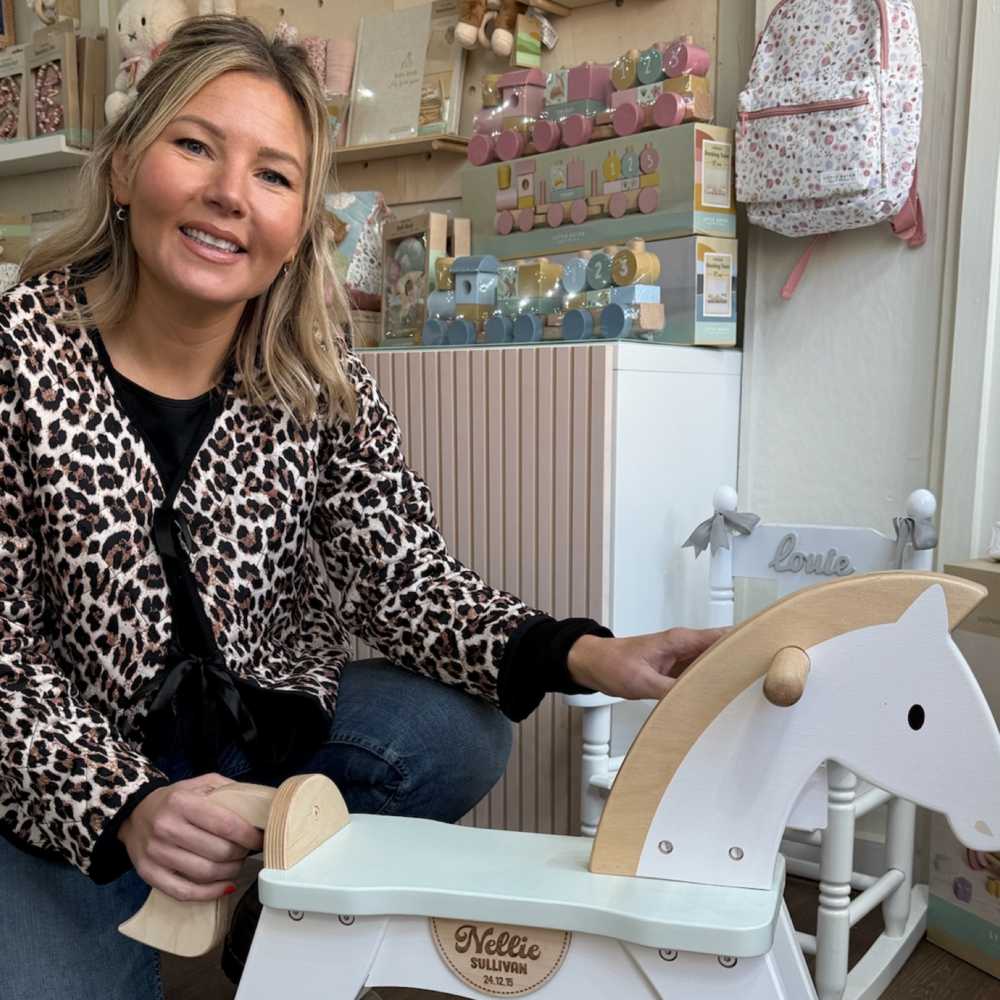 A lady knelt beside a white rocking horse in the Nellie's Keepsake Co. shop 