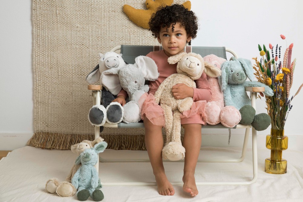 A child on a chair holding and sitting beside soft toys