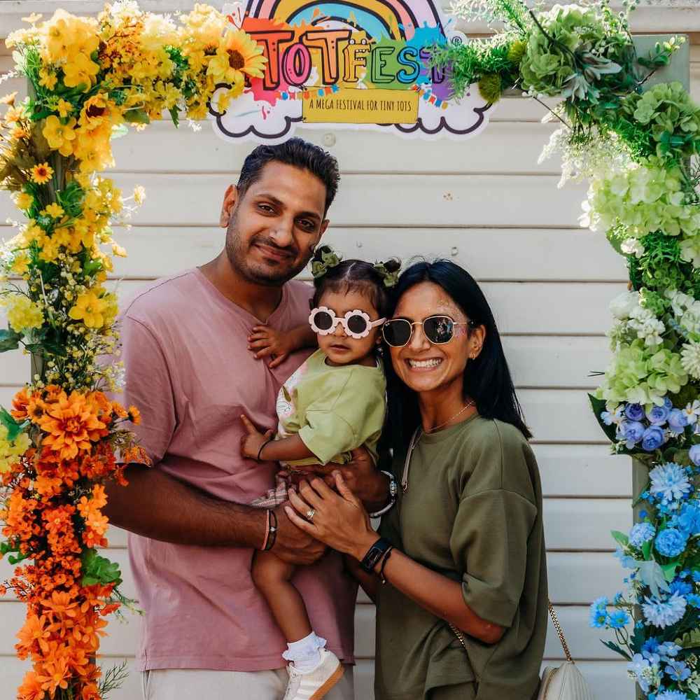 A couple holding a small child beneath an arch of flowers and a TOTFest sign 