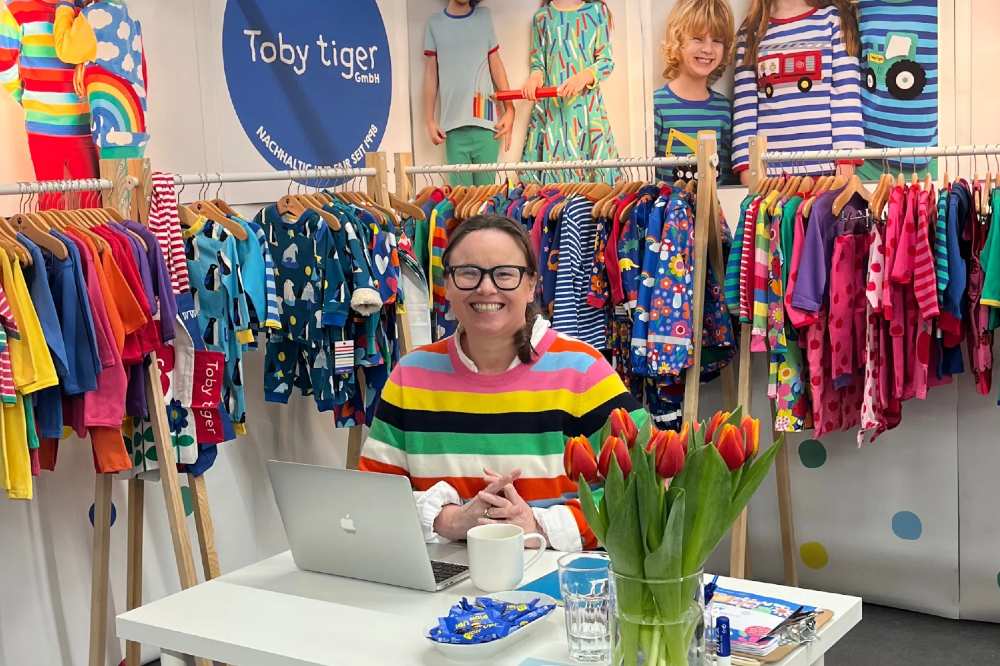 The founder of Toby Tiger sat at a desk amongst rails of Toby Tiger children's clothes