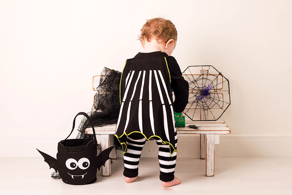 A young girl in a Halloween costume stood next to a wooden bench playing with a toy