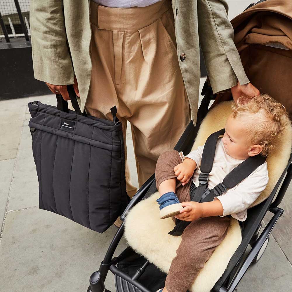 A mother stood next to a toddler in a pram holding a eco stroller caddy