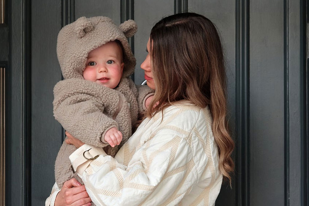 A mother holding a baby wearing a grey pramsuit