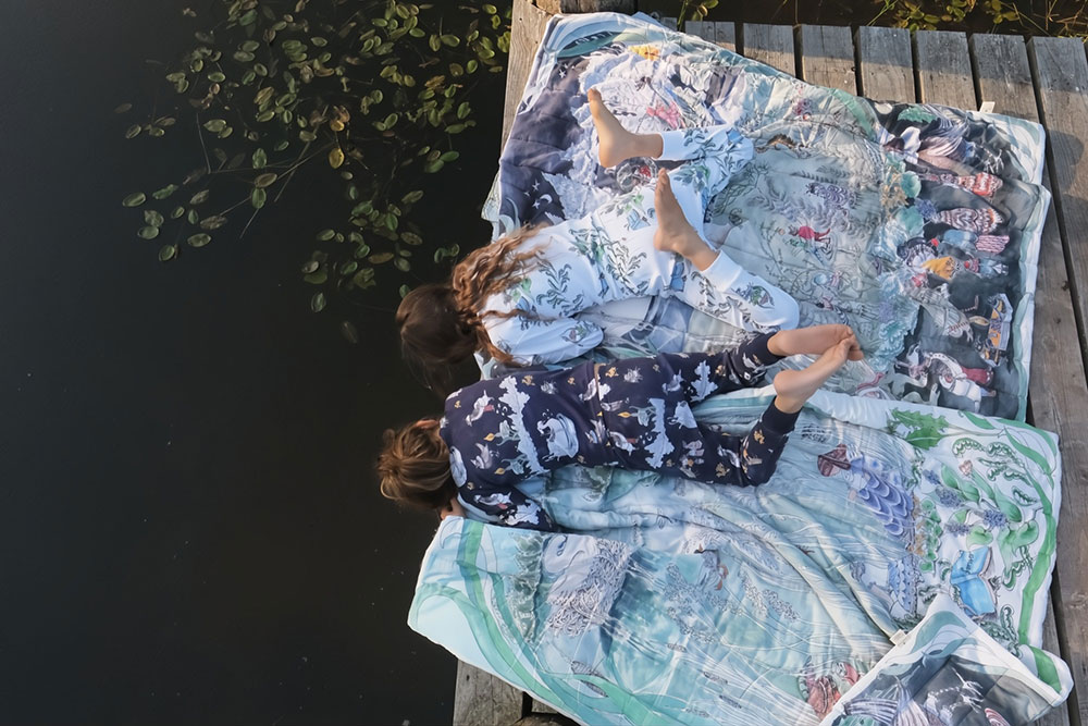 Two young girls laid on blankets looking into a pond.