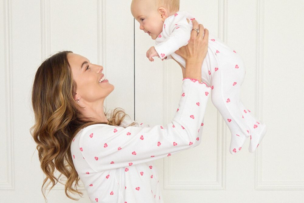 A mother holding a baby in the air wearing matching pyjamas