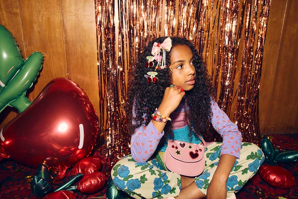 A young girl sat on the floor wearing a pink handbag and jewellery in her hair