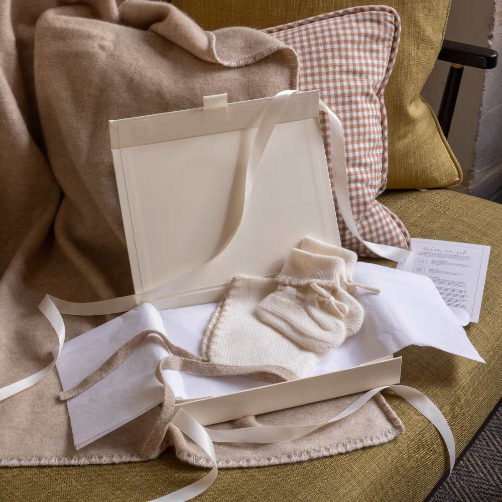 An Avery Row cashmere baby gift set displayed in a gift bow on a sofa 