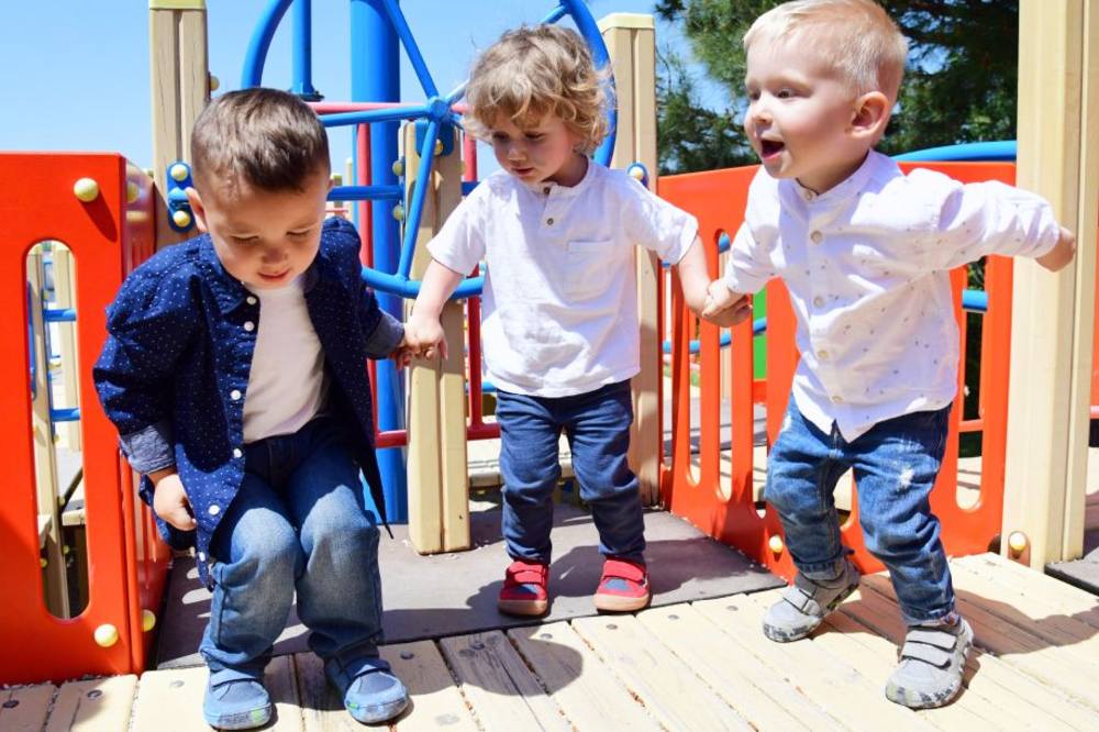 Three young children outide jumping on a climbing frame 