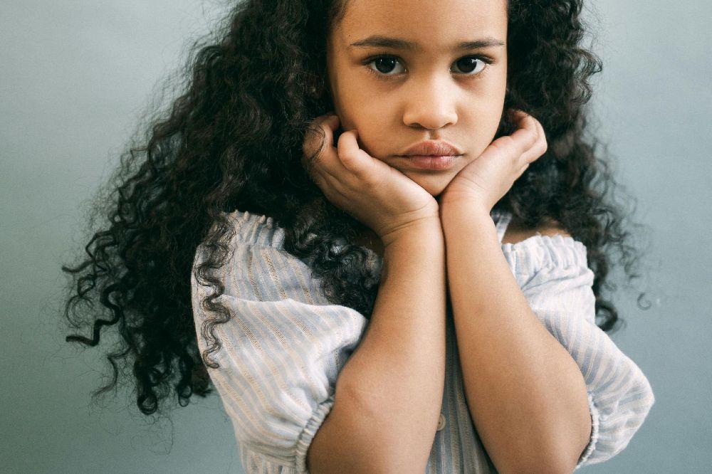 A girl with long dark curly hair with her hands to her face