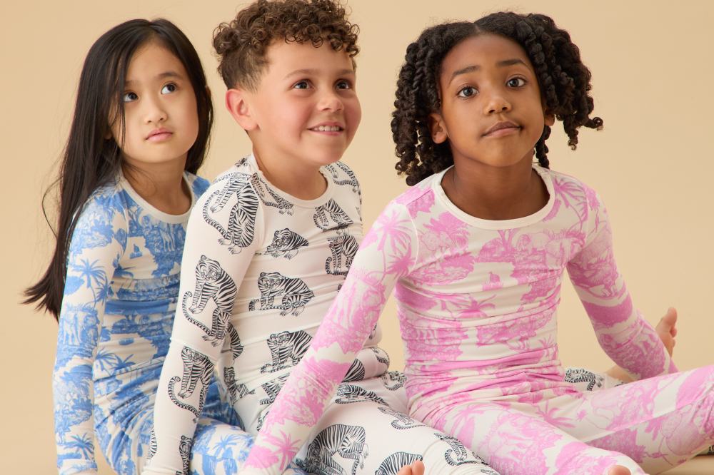 Three children sat on the floor in a row wearing pyjamas from the MORI x Desmond Dempsey collection