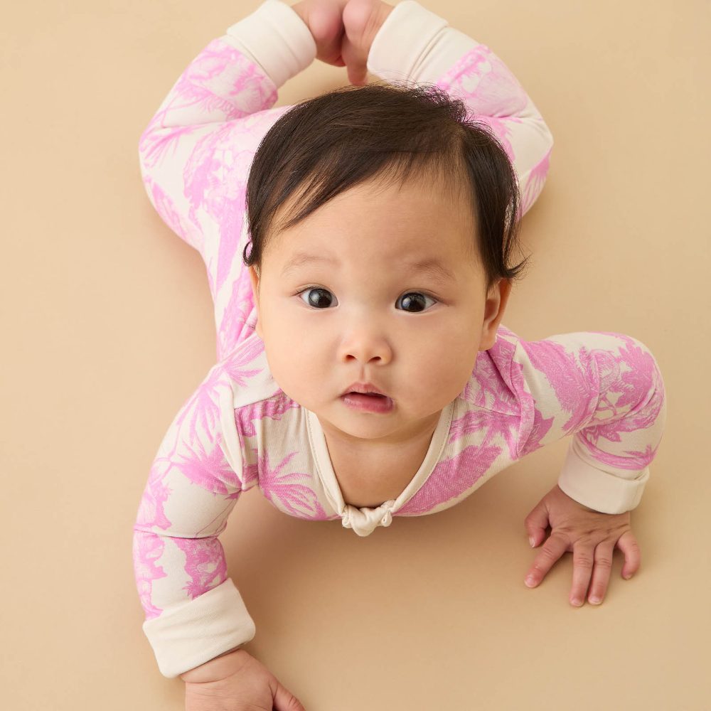 A baby wearing a pink and white print sleepsuit from the MORI x Desmond Dempsey collaboration 