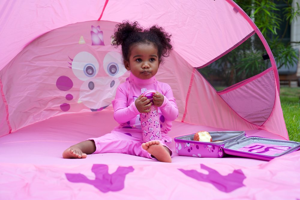 A girl sat outside beneath a pink character sun shade by Go Outdoors and My Carry Potty