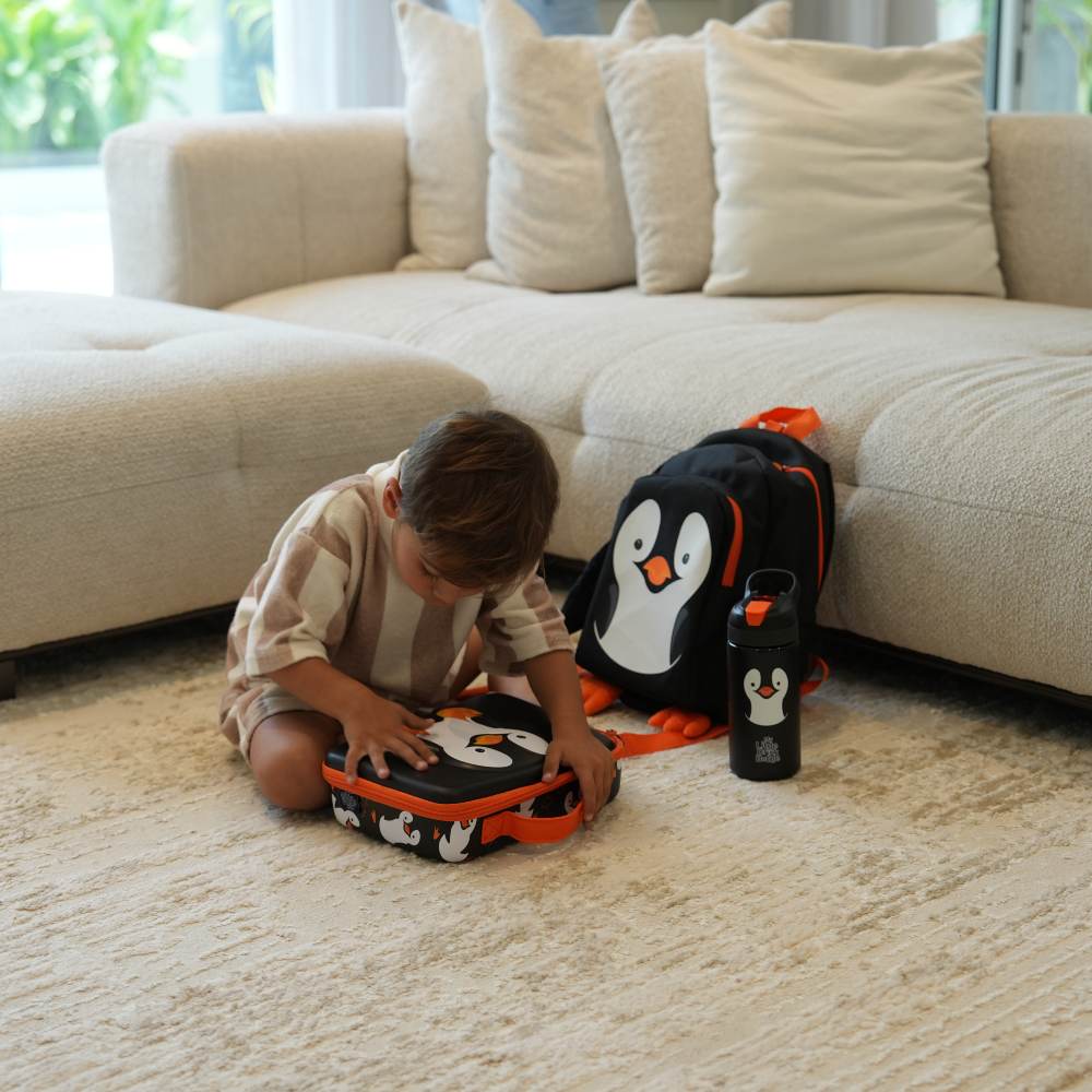 A young child sat on the floor of a room with a penguin backpack, bottle and lunch bag by GO Outdoors and My Carry Potty 