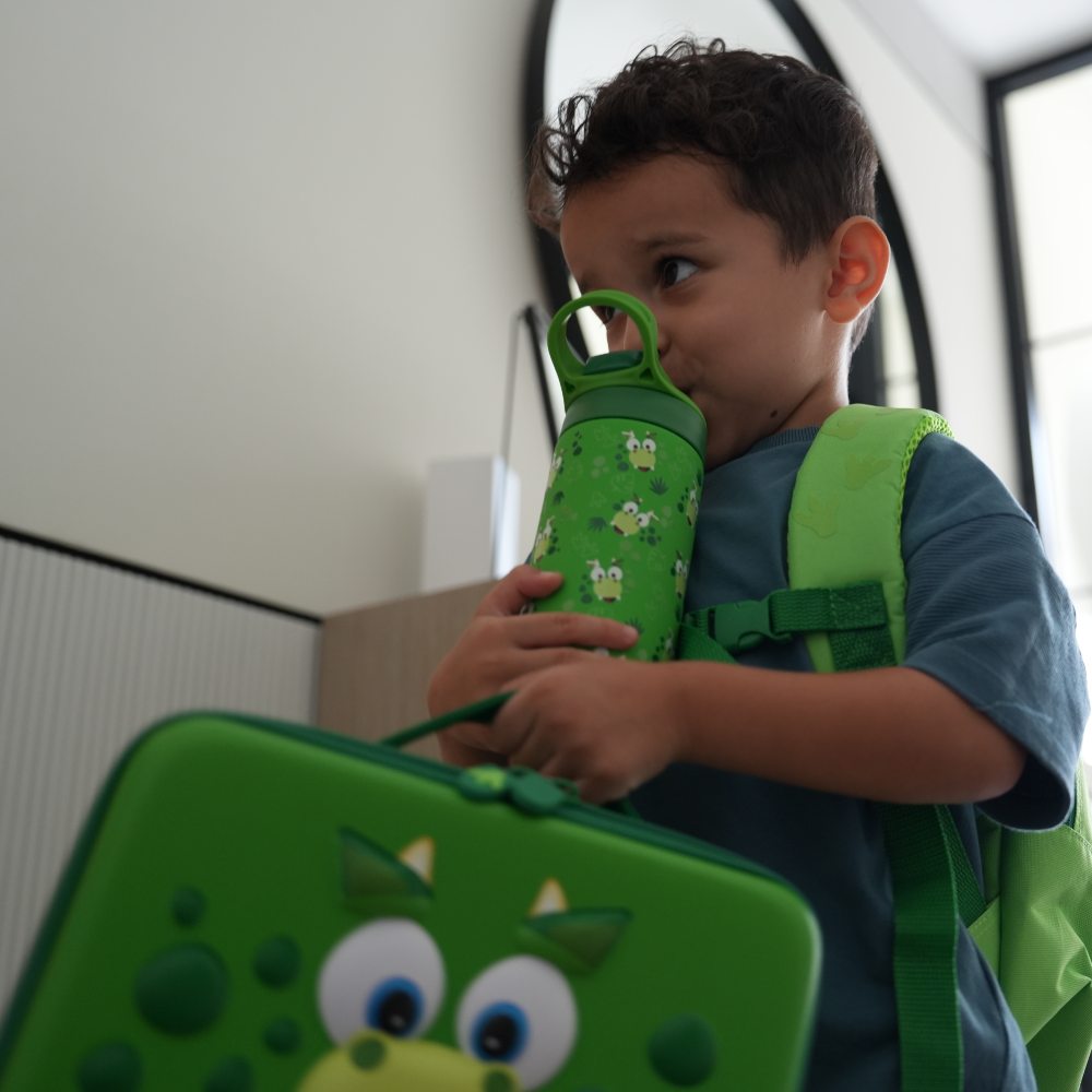 A boy carrying a green character lunchbag with a matching rucksack on his back from the GO Outdoors and My Carry Potty range 