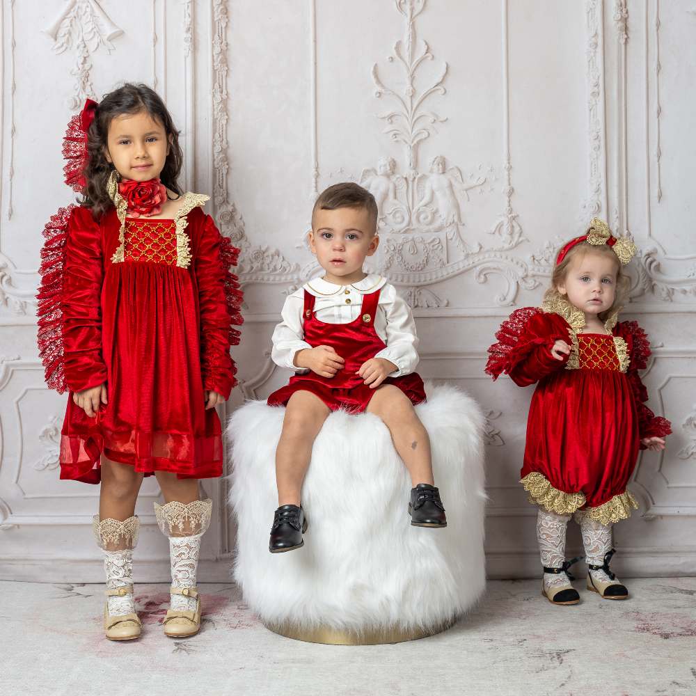 Three young children in an ornate room wearing luxurious red occasionwear outfits by Petite Maison Kids