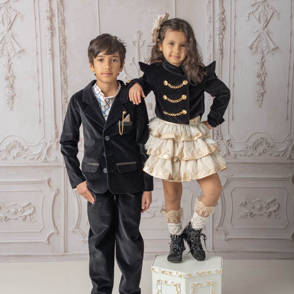 A young boy stood by a girl on a podium wearing luxurious coordinating black outfits by Petite Maison Kids