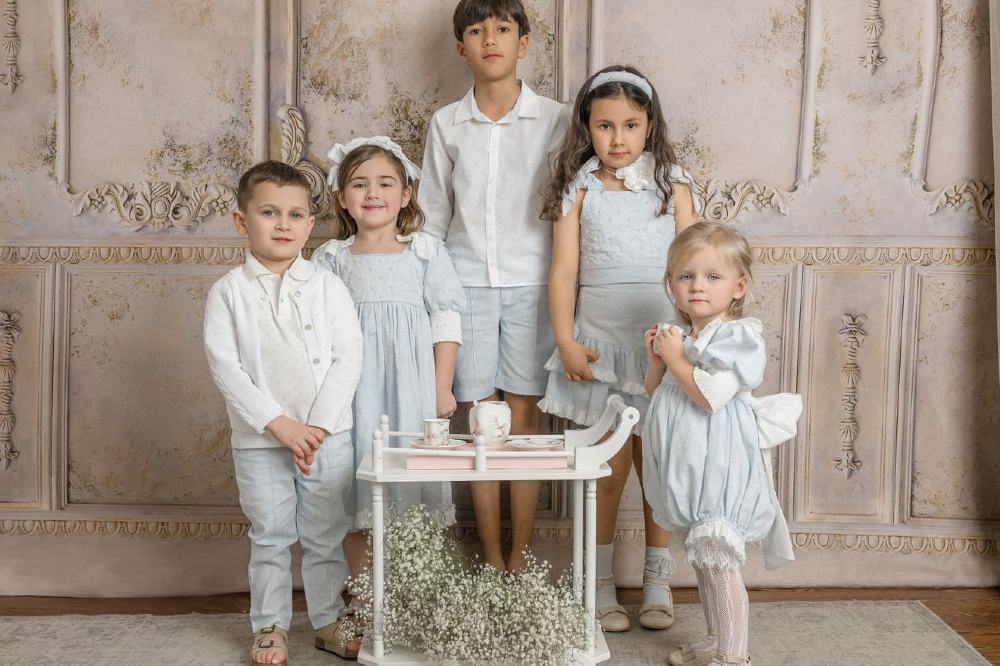 Five children stood in an ornate room wearing coordinating pale blue outfits by Petite Maison Kids