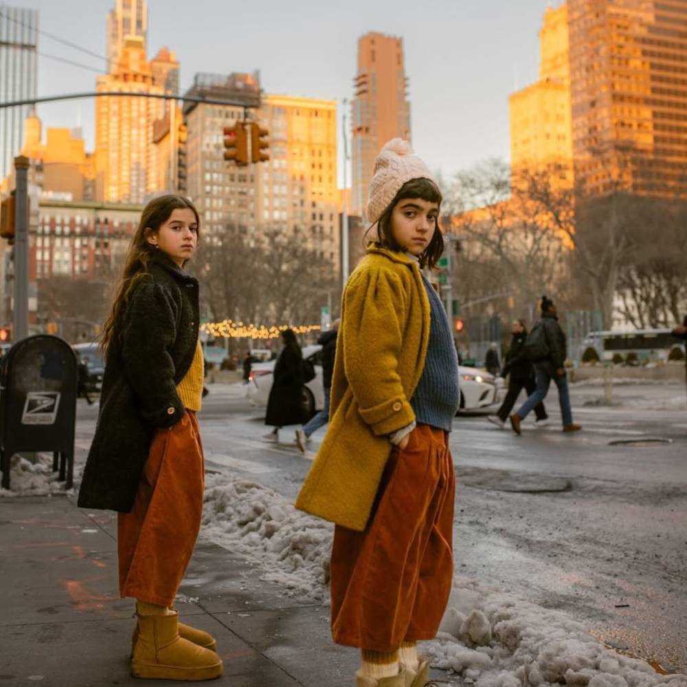 Two girls in winter clothes stood on the curb of a snowy street in New York 