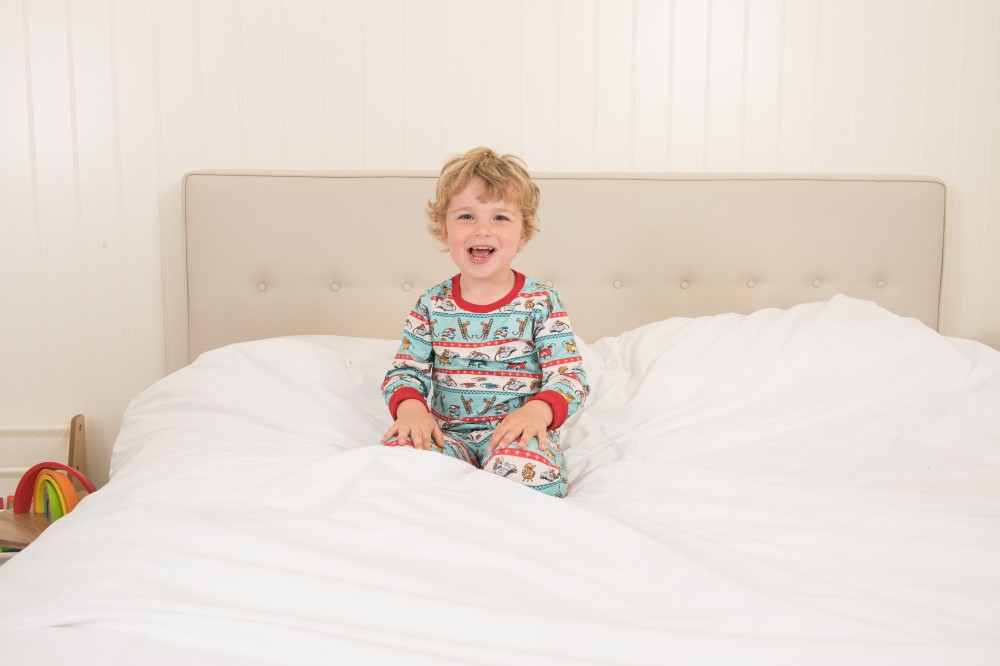 A young child sat on a bed smiling wearing pyjamas from the new Ducky Zebra x Roald Dahl range
