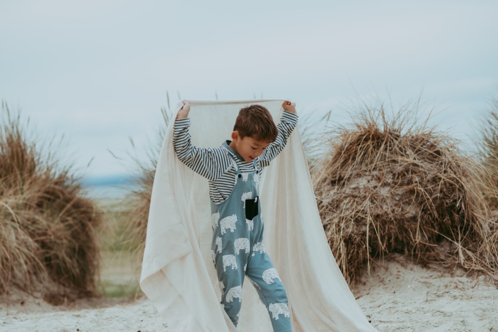 A child on a beach holding a blanket above his head