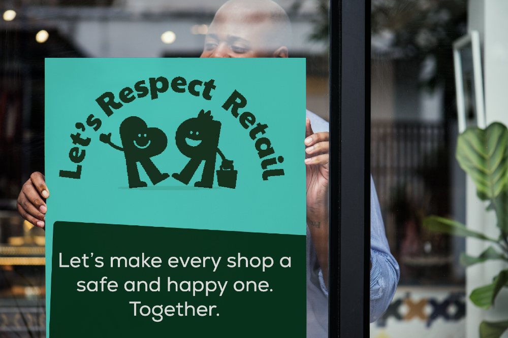 Someone putting a Let's Respect Retail poster in a shop window 