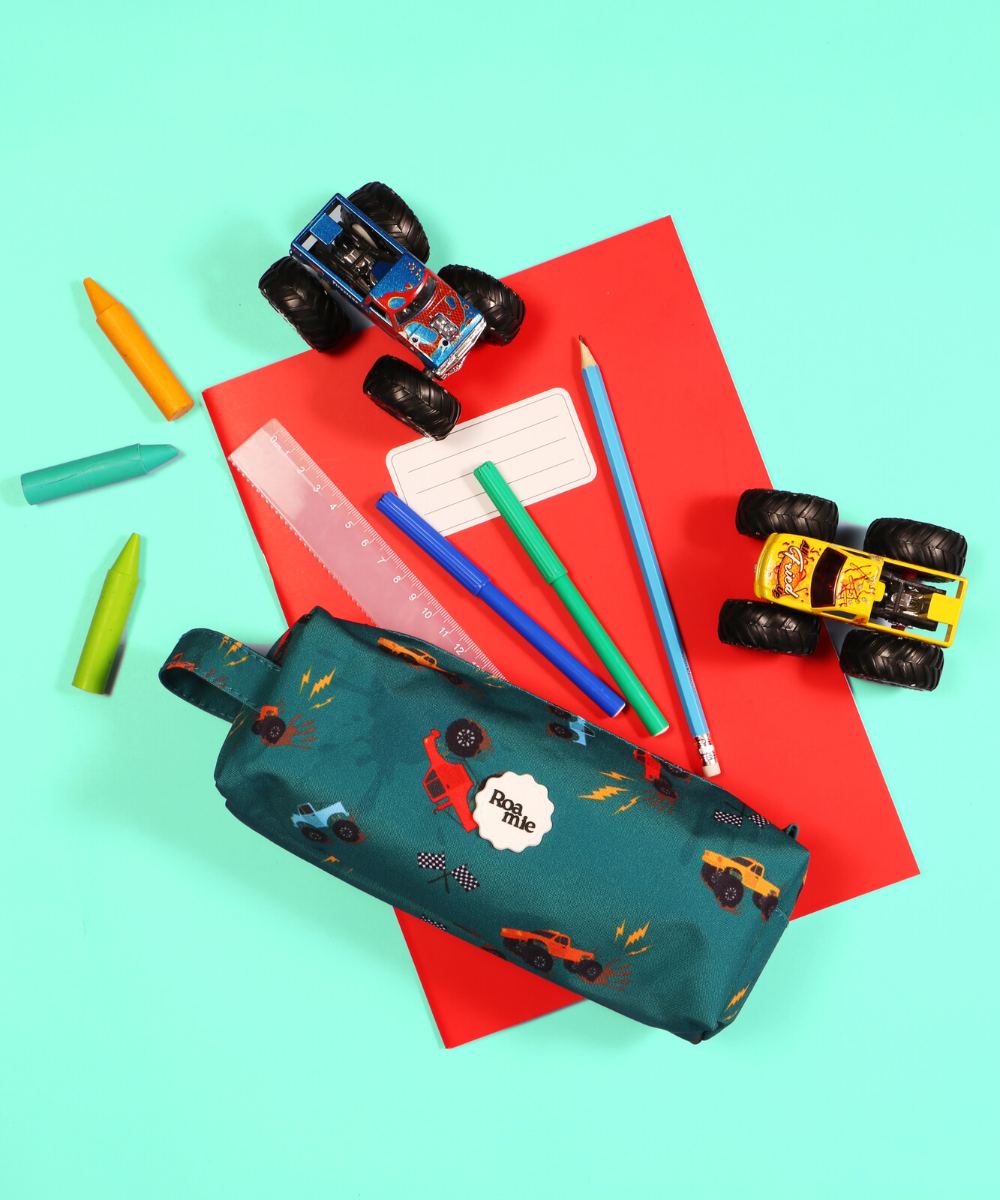 A Roamie monster truck print pencil case displayed with a notebook, pens and toy trucks 