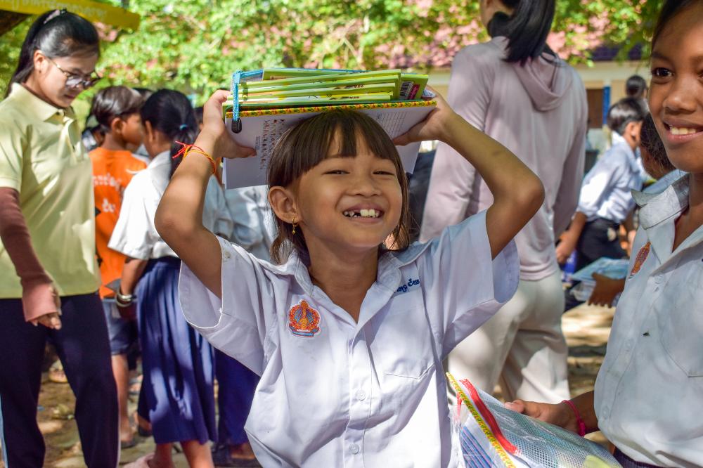 A Cambodian school girl smiling and holding a book above her head