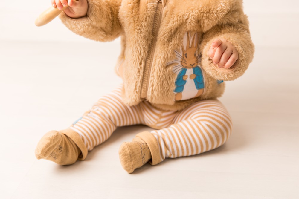 A child sat on the floor wearing a fluffy hoodie and leggings from Blade & Rose's Peter Rabbit Neutral collection