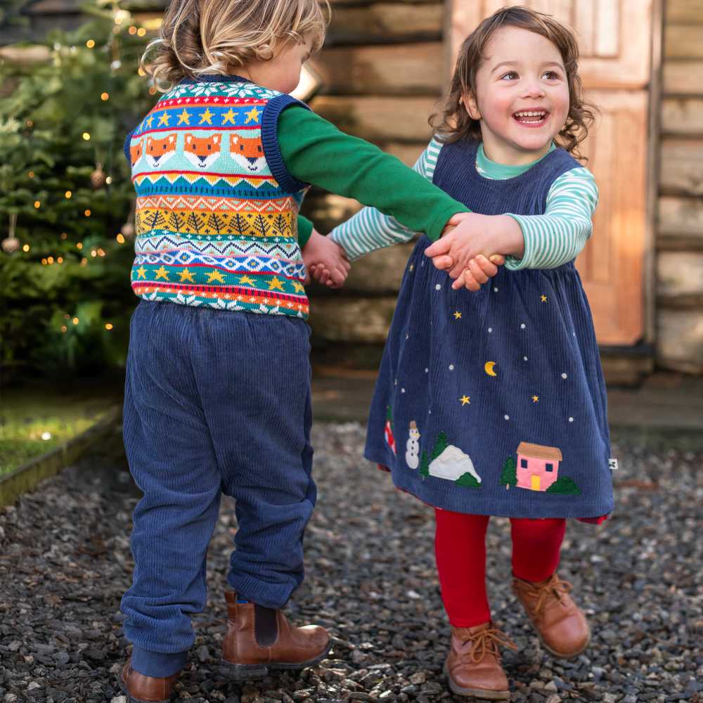 Two children dancing holding hands outside wearing outfits from Frugi's Tales from the Glen collection