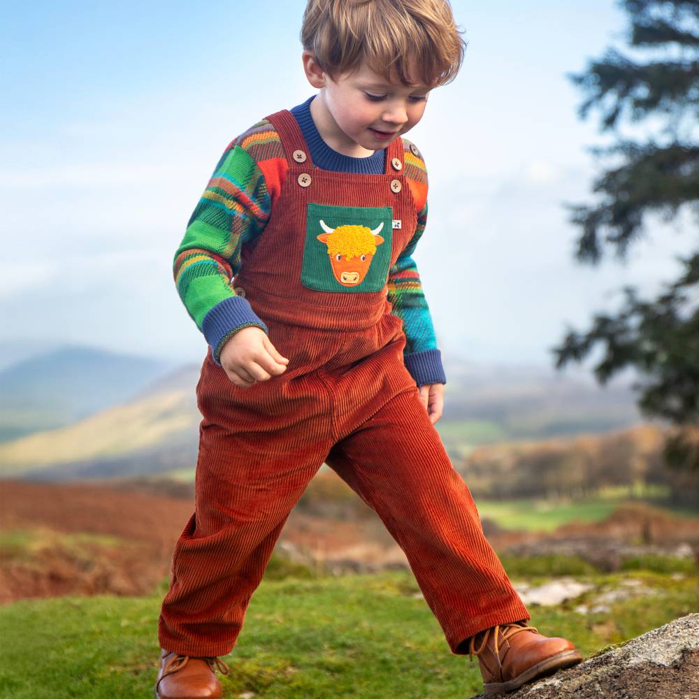 A young boy outside walking in the hills of Scotland wearing dungarees and a top from Frugi's Tales from the Glen collection