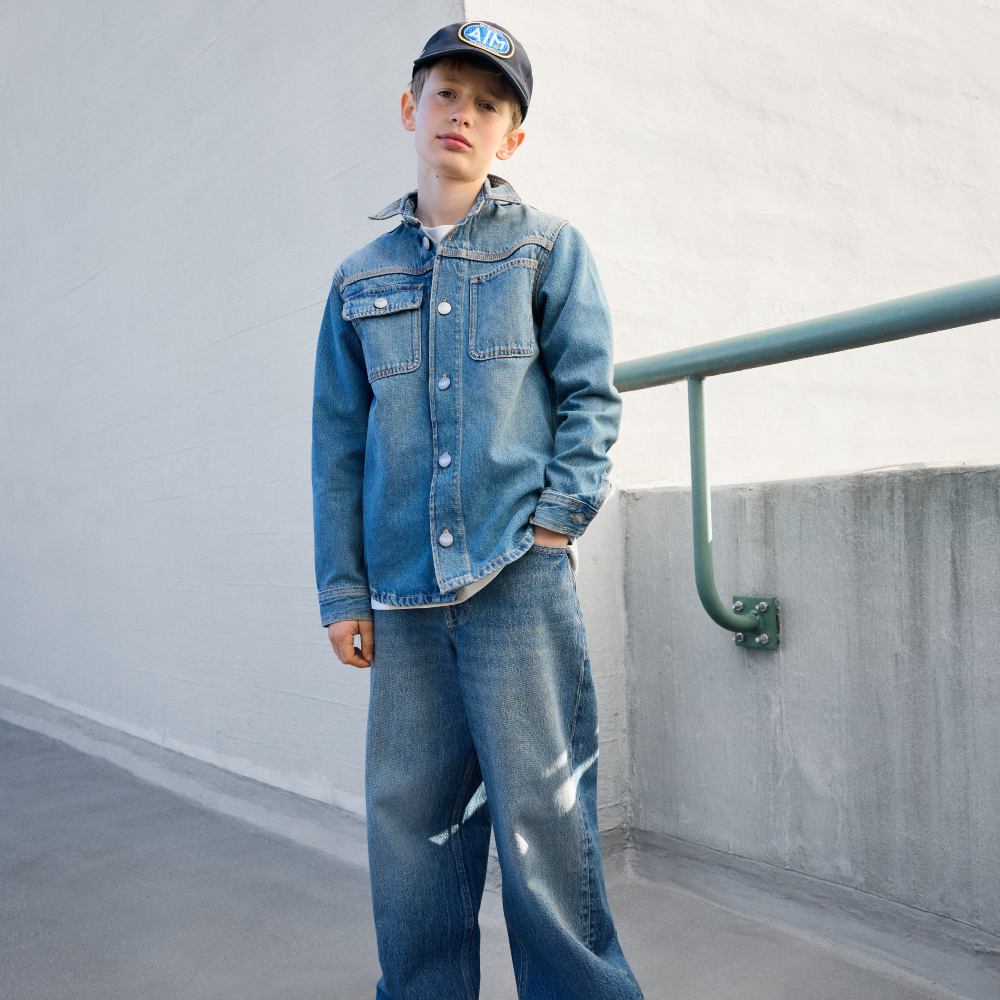 A bot dressed all in denim stood outside beside a concrete wall 